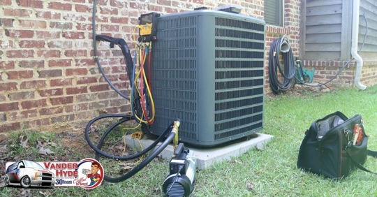 An air conditioning condenser with tools surrounding on grass next to a brick wall