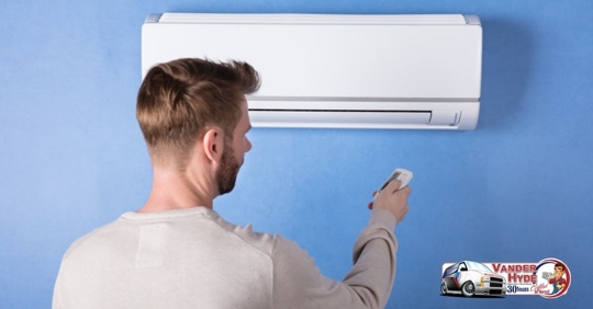 a man pointing a remote at a wall-mounted ductless mini split on a blue wall